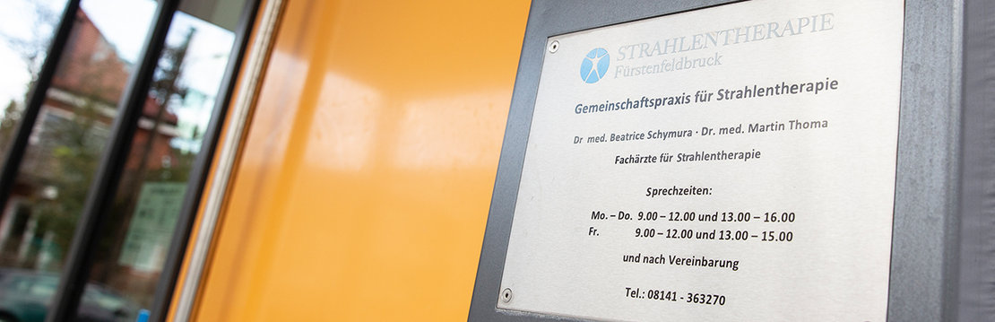 Praxisschild Gemeinschaftspraxis für Strahlentherapie Fürstenfeldbruck mit orangener Tür.