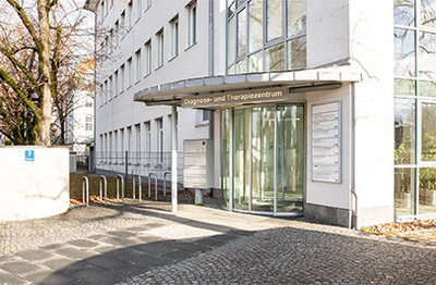 Eingang Strahlentherapiepraxis Nymphenburg mit Glastür halbrund draußen.