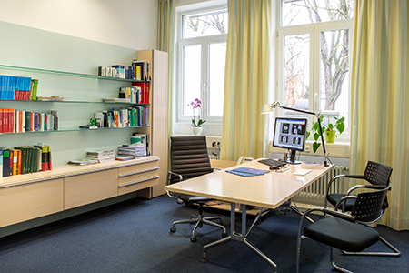 Besprechungsraum mit Schreibtisch, Stühlen, Bücherregal und PC.